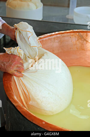 Pastore casaro raccoglie il formaggio dal grande paiolo di rame con il latte di vacca e latte di capra Foto Stock