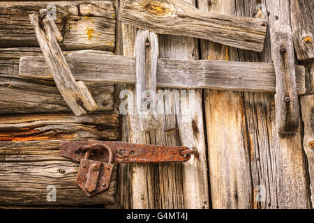 Un vecchio log in legno porta è chiuso, bloccato e bloccato con un fascio di log e un arrugginito pick serratura in ghisa. Foto Stock