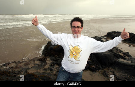 Adam Hayes, 26, sulla spiaggia di Castlerock, a Co Londonderry, celebra dopo aver imparato che sarà uno dei portatori regionali di torcia olimpica. Foto Stock