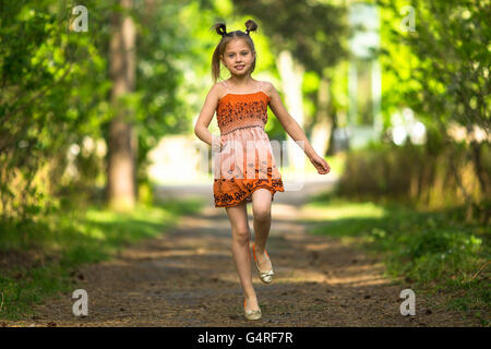 Allegro bambina che corre lungo un percorso in un parco. Foto Stock