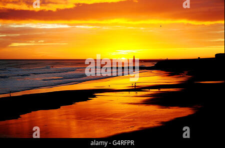 La gente cammina sulla spiaggia durante l'alba su Tynemouth Longsand, a Tynemouth, Tyne e indossare. Foto Stock