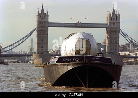 Le gondole che pendono dal London Eye, fanno il loro viaggio in barca lungo il Tamigi nel centro di Londra, arrivando al Tower Bridge, prima di andare sul sito della ruota gigante. Le 32 capsule possono impiegare fino a mezz'ora per viaggiare intorno alla ruota. Con un peso di 1.5 tonnellate e costruiti in Francia dalla compagnia di skilift Poma, le capsule offrono ai passeggeri una vista panoramica fino a 25 miglia di distanza. Foto Stock