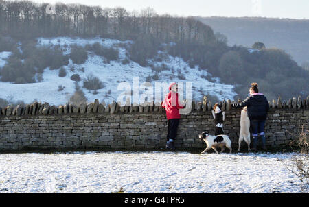 Gli escursionisti e i loro cani ammirano la vista dal Crickley Hill Country Park, Gloucestershire, come il paese si è bracchiato per un periodo di tempo più fresco che ha portato la neve in alcune regioni. Foto Stock