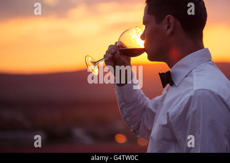 Elegante giovane ragazzo beve vino sul campo di lavanda al tramonto Foto Stock