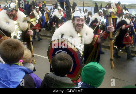 La 'squadra Jarl' di guizzatori - Shetlanders vestito in costume vichingo - marcia attraverso le strade di Lerwick nelle Isole Shetland mentre consegnano la galey, una longship di legno di 30 piedi, al porto come parte del tradizionale festival pagano di Up Helly AA. La cucina sarà bruciata dai guizzatori in una cerimonia. Foto Stock