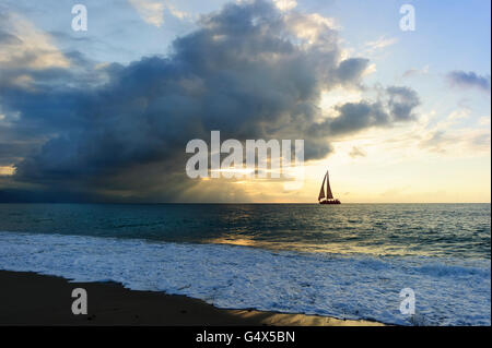 Barca a vela al tramonto fasci di Sun è un burst raggi di sole con la ripresa attraverso le nuvole come una barca a vela si sposta lungo l'acqua verso la l Foto Stock