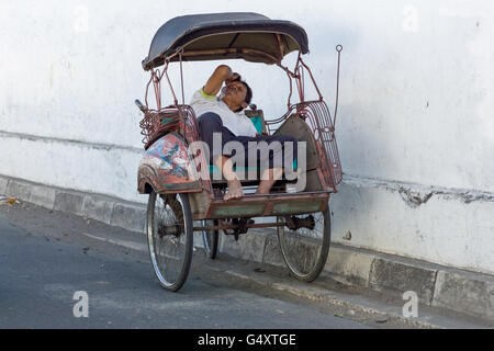 Indonesia, Java, Yogyakarta, scene di strada - dormire rickshaw conducente Foto Stock