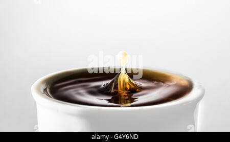 Goccia di spruzzi di latte in una tazza di caffè nero Foto Stock