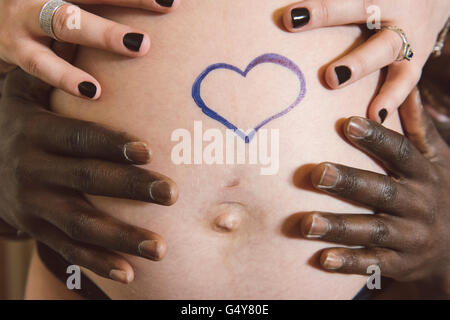 I genitori a essere stanno tenendo le mani sul ventre in gravidanza; cuore disegno sul ventre. Foto Stock