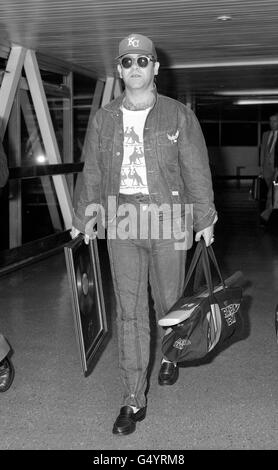 La rock star inglese Elton John ritorna a Londra all'aeroporto di Heathrow dopo essere arrivata dall'Australia. È stato in Australia guardando la squadra inglese di cricket, ed è tornato con un bat in cima alla sua borsa, firmato da entrambe le squadre Foto Stock