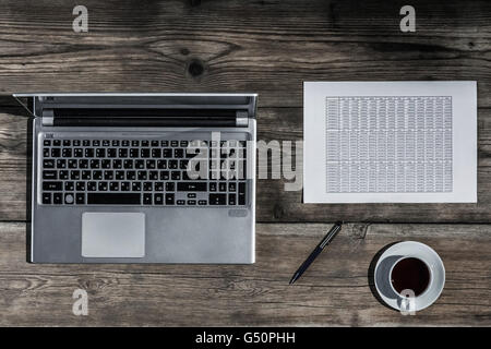 Il luogo di lavoro con un tavolo di legno con il computer portatile, documenti e caffè su di esso Foto Stock