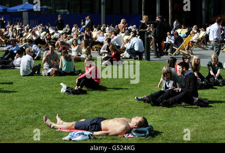 Un uomo giace sull'erba con la sua camicia rimossa come i membri del pubblico godere del sole in Spinningfields nel centro della città di Manchester. Foto Stock