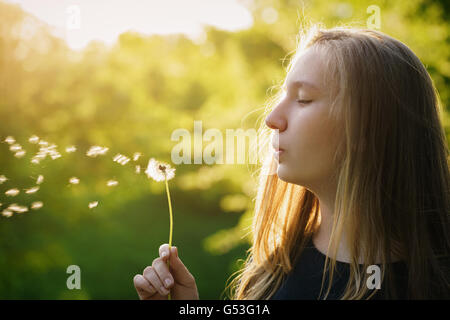 Teen girl soffiando tarassaco nella luce del tramonto Foto Stock
