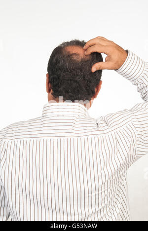 Vista posteriore di un uomo con una macchia calva in piedi contro uno sfondo bianco Foto Stock