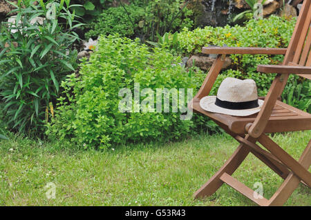 Cappello di paglia in una sedia di legno in un giardino verde Foto Stock