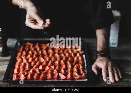 Lo chef maschio salatura giù i pomodori su un vassoio. Preparare i pomodori ciliegia per la tostatura Foto Stock