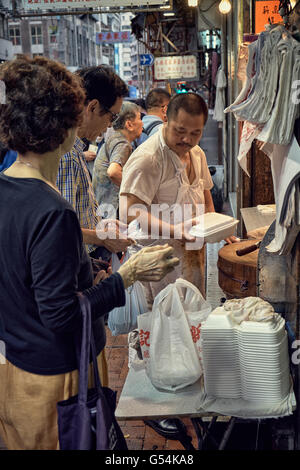 I clienti in coda e l'acquisto delle selezioni di portar via il cibo cotto in un negozio di Shanghai Street in Yau Ma Tei, Hong Kong. Foto Stock