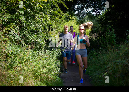 Tre persone di diverse età in esecuzione all'aperto lungo un sentiero di bosco. Foto Stock