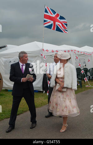 Sulla brughiera al Royal Ascot, una coppia elegantemente vestita e alla moda si gode una giornata di corse di cavalli. Bandiera Union Jack. Il lato Heath dell'ippodromo è molto più economico o gratuito. 2016 2010 HOMER SYKES Foto Stock