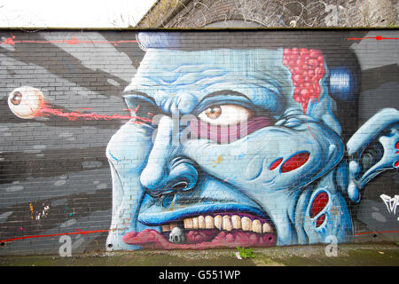 Graffiti e arte di strada dipinto su un muro di mattoni di un volto di uomo con il suo bulbo oculare fuoruscita Foto Stock