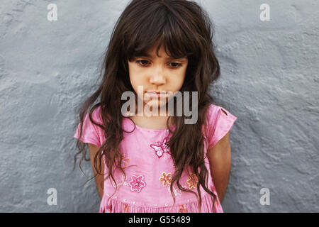 Close up ritratto di bambina in piedi che guarda sconvolto. Triste ragazza in piedi contro un muro grigio. Foto Stock