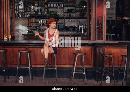 Ritratto di elegante femmina giovane seduto in un bar con bevande e guardando lontano. Bella femmina caucasica presso la caffetteria counte Foto Stock