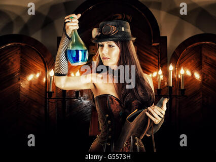 Alchemist. Bella brunete donna strega che indossa lo stile steampunk prepara una pozione di veleno o in un segreto laboratorio occulto e legge Foto Stock