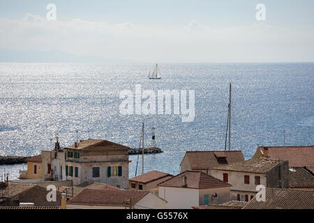 Vista sui tetti delle case di Gaios Paxos grecia con yacht della vela sul luccicante Oceano soleggiato in background Foto Stock