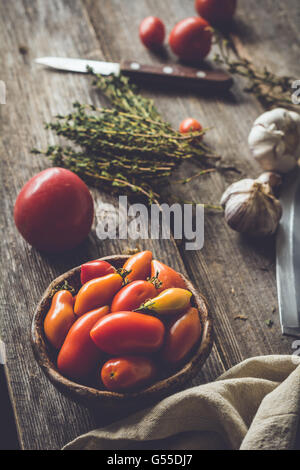 Cimelio di pomodori, banco di timo molle, aglio e coltello su tavola in legno rustico. Rustico atmosferica ancora la vita di pomodori Foto Stock