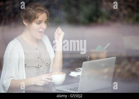 Ritratto di giovane sconvolto felice bellissima femmina in seduta urbana moderna caffetteria con pc notebook, a bere caffè e alla ricerca Foto Stock