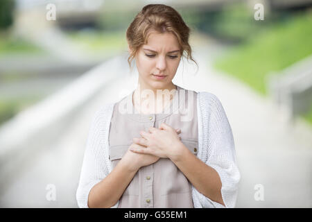 Ritratto di sottolineato bella donna che cammina sulla strada e toccando il suo torace con espressione triste o avere mal di cuore Foto Stock