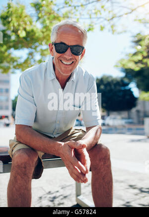 Ritratto di sorridere senior tourist seduti all'aperto su un banco di lavoro. Maschio maturo turistico con occhiali da sole rilassante nella città su un su Foto Stock