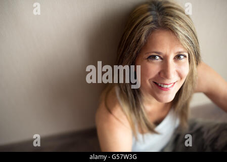 Unica bella donna matura in camicia senza maniche con capelli lunghi guardando verso l'alto con piacevole sorriso e spazio di copia Foto Stock