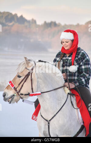 Serie di immagine di una ragazza con il suo fiordo norvegese cavallo, entrambi in xmas outfit equitazione in un paesaggio invernale Foto Stock