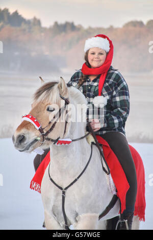 Serie di immagine di una ragazza con il suo fiordo norvegese cavallo, entrambi in xmas outfit equitazione in un paesaggio invernale Foto Stock