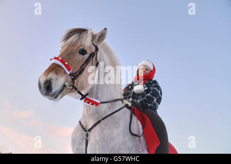 Serie di immagine di una ragazza con il suo fiordo norvegese cavallo, entrambi in xmas outfit equitazione in un paesaggio invernale Foto Stock