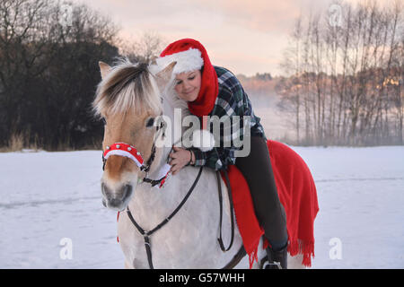 Serie di immagine di una ragazza con il suo fiordo norvegese cavallo, entrambi in xmas outfit equitazione in un paesaggio invernale Foto Stock