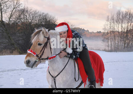 Serie di immagine di una ragazza con il suo fiordo norvegese cavallo, entrambi in xmas outfit equitazione in un paesaggio invernale Foto Stock