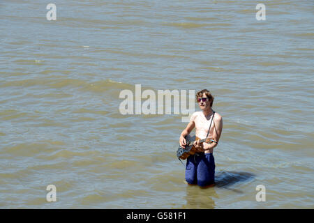 Busker divertente folle su London South Bank a suonare la chitarra mentre in piedi nel fiume Tamigi Foto Stock