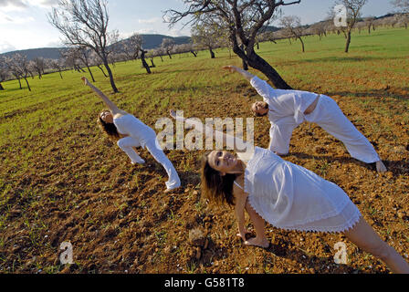 Tre persone, uno svedese uomo, una donna brasiliana e una donna spagnola, la pratica dello yoga nei campi di Ibiza, Spagna Foto Stock