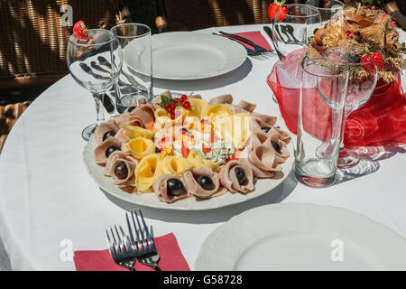 Piastra fredda con prosciutto e formaggio e frutta. Tabella decorate in bianco e rosso in giardino Foto Stock