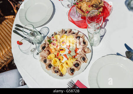 Piastra fredda con prosciutto e formaggio e frutta. Tabella decorate in bianco e rosso in giardino Foto Stock