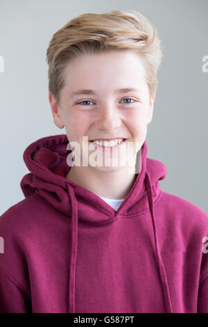 Ragazzo adolescente in una felpa con cappuccio di borgogna. Egli sorride per la fotocamera. Foto Stock