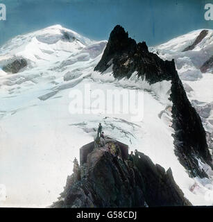 Das Hotel liegt nicht auf dem höchsten Punkte der Felsen, vielmehr bedarf es einer kleinen Kletterei, um ihren Gipfel zu erreichen. Der Rundblick hier ist etwas umfassender, namentlich erscheint der Montblanc noch freier. Das Gestein stürzt nahezu senkrecht zur Tiefe und verschwindet dann unter dem zerrissenen Eisstrome des oberen Bossons-Gletschers, sodass die Felsen der Grands mUlets wie eine Insel vom Eise umflossen sind. Nach eingenommener Mahlzeit, die bei den Schwierigkeiten des Transports der Lebensmittel ganz vortrefflich und nicht allzu teuer ist, beobachten wir vor der Hütte stehend n Foto Stock