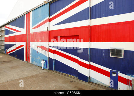 Il pittore Rob Saunders dipinge le gigantesche porte dell'hangar a Venture Quays a East Cowes sull'Isola di Wight in previsione della visita della Regina all'isola il mese prossimo. Foto Stock