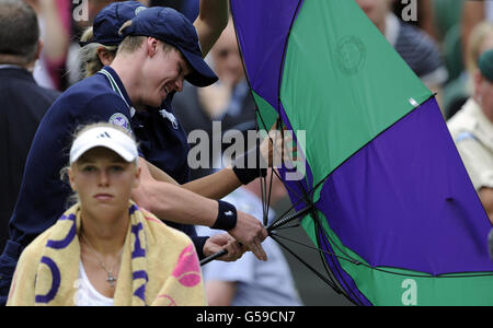 Il danese Caroline Wozniacki attende come un ragazzo di palla tenta di aprire un ombrello durante il terzo giorno dei Campionati di Wimbledon 2012 all'All England Lawn Tennis Club di Wimbledon. Foto Stock