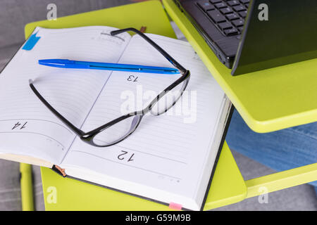 Paio di Occhiali giacente sul laptop tavolo vicino a aprire una pagina vuota di un business journal o diario con una penna per appuntamenti, organizzando un calendario o agenda. Foto Stock