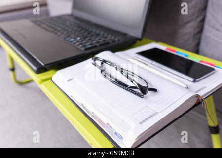 Focus sui bicchieri giacente sul laptop tavolo vicino a aprire una pagina vuota di un diario con una penna per appuntamenti, organizzare una pianificazione. Foto Stock