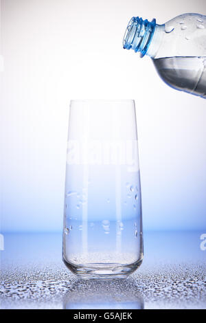 La bottiglia di plastica con acqua in vuoto bicchiere con la riflessione su gocce di acqua su bianco e lo sfondo blu Foto Stock