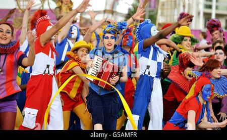 La vista che saluta gli atleti e gli ufficiali in arrivo da tutto il mondo, presso il loro Villaggio Olimpico di Londra Est, dove i membri del Teatro Nazionale della Gioventù Britannica li accolgono con routine di canto e danza, con una settimana fino all'inizio delle partite di Londra 2012. Foto Stock